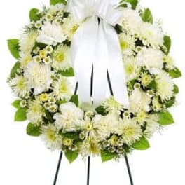 White floral wreath with a large white ribbon on a stand