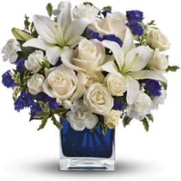 White lilies and roses with blue accents in a cobalt glass cube vase
