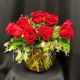 Red roses arranged in a round glass vase with greenery