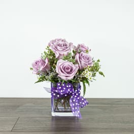 Lavender roses in a square glass vase with a purple polka-dot ribbon