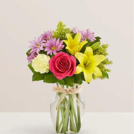 Mixed bouquet in a clear glass vase with a pink rose and yellow lilies
