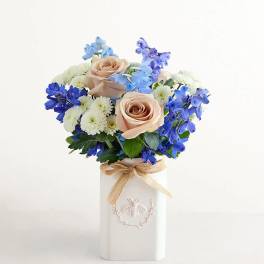 Bouquet of peach roses, blue flowers, and white daisies in a white vase