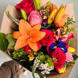 Colorful bouquet with roses, lilies, and mixed blooms wrapped in brown paper