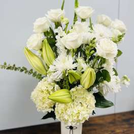 White floral arrangement with roses, lilies, and hydrangeas in a white vase