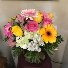 Pink and yellow roses with gerbera daisies in a glass vase