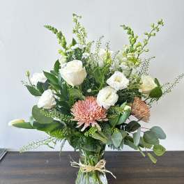 Mixed arrangement of white roses, snapdragons, and peach chrysanthemums in a clear glass vase