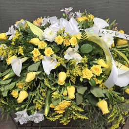 Yellow roses and white lilies arranged in a large sympathy spray with ribbon