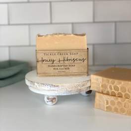 Bar of honey hibiscus soap on a small stand beside two honeycomb-patterned soap bars