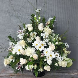 Large white floral arrangement with roses and daisies in a black vase