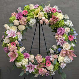 Large floral wreath with pink, white, and green flowers on a black stand