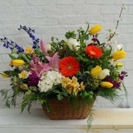 Mixed flower arrangement in a wicker basket with pink, yellow, white, and orange blooms