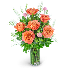 Orange roses in a clear glass vase with pink pom-pom accents