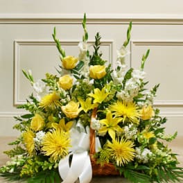 Yellow and white floral arrangement in a wicker basket with a white ribbon
