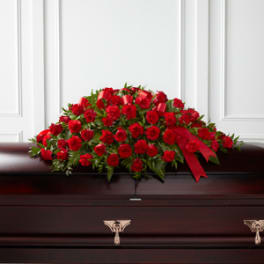 Red rose casket spray with a red ribbon on a dark wood casket