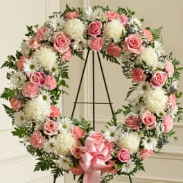 Pink and white floral wreath on a black stand with a pink bow