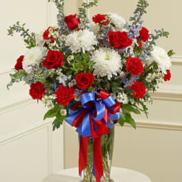 Red roses and white chrysanthemums in a glass vase with a red and blue ribbon