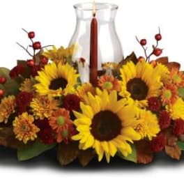 Sunflower and autumn flower arrangement around a glass hurricane candle holder