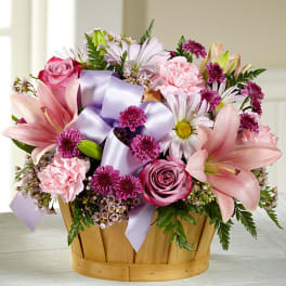 Pink and lavender flower arrangement in a wooden basket with ribbon