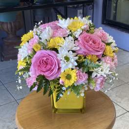 Pink roses, yellow and white daisies, and carnations in a yellow vase