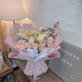 Pastel bouquet of mixed flowers wrapped in pink paper with a birthday topper