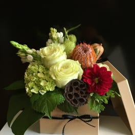 Mixed floral arrangement in a kraft box with white roses and a red bloom