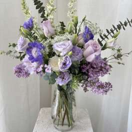 Tall lavender and white flower arrangement in a clear glass vase.