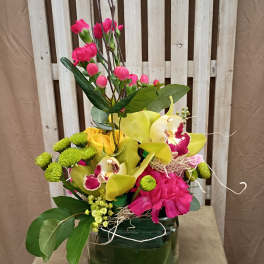 Mixed floral arrangement in a green glass vase with yellow orchids and pink blooms