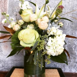 Mixed bouquet of pale roses, lilies, and white hydrangea in a glass vase
