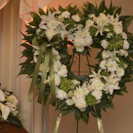 White floral wreath with a green ribbon on a stand