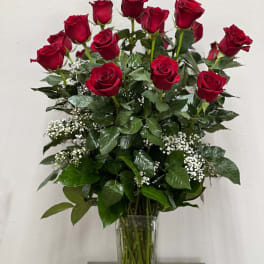 Red roses arranged in a clear glass vase with white filler flowers.