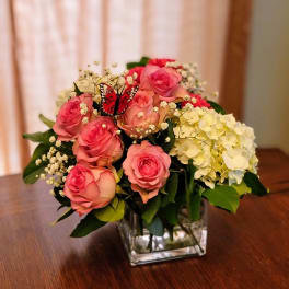 Pink roses and white hydrangeas in a square glass vase with a butterfly accent