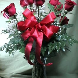 Red roses in a clear glass vase with a large red ribbon