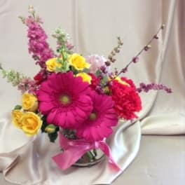 Pink gerbera daisies and yellow roses in a glass vase with a pink ribbon