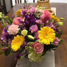 Mixed bouquet of pink, yellow, and purple flowers in a glass vase