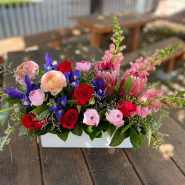 Mixed bouquet in a white rectangular vase with red, pink, purple, and peach flowers