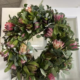 Large wreath with pink protea and mixed greenery on a white door