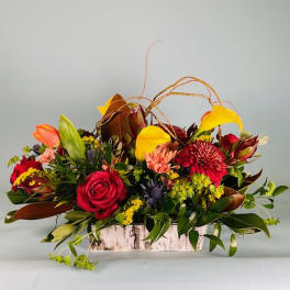 Mixed floral arrangement in a rustic rectangular container with red, yellow, and orange blooms