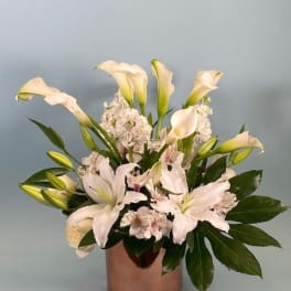 White calla lilies and pale pink flowers arranged in a copper vase