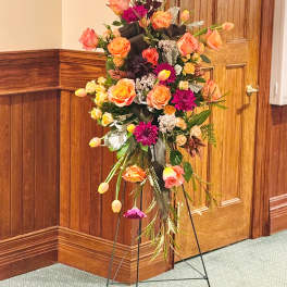 Tall floral standing spray with orange and pink blooms on an easel