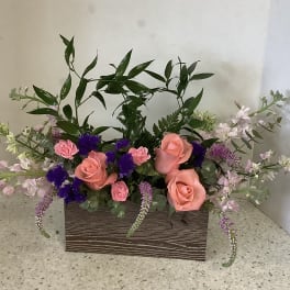 Pink roses and purple flowers arranged in a rectangular wooden box