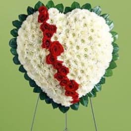 Heart-shaped floral tribute with white flowers and a red rose stripe on an easel
