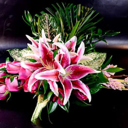 Pink roses and stargazer lilies arranged with greenery on a dark surface.