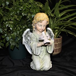 Angel figurine holding a small bird, with potted plants behind it
