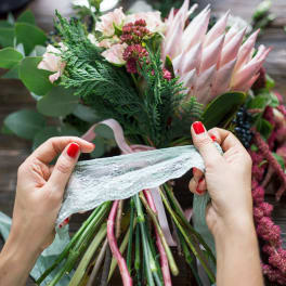 Hands tying lace around a pink and green bouquet