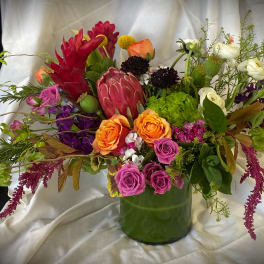Mixed bouquet in a green glass vase with orange, pink, purple, and white blooms