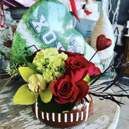 Red roses and yellow orchids in a football-shaped vase with a glitter heart pick