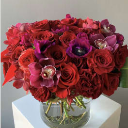 Red and pink bouquet of roses and orchids in a clear glass vase