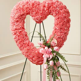 Pink heart-shaped floral wreath on an easel with a small rose bouquet