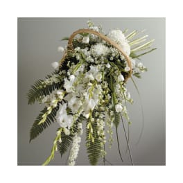 Tall white funeral spray in a wicker basket on an easel with cascading blooms and ferns.