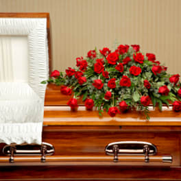 Casket spray of red roses resting on a polished wooden casket with white interior lining
